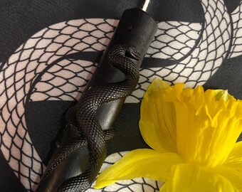 May include: Black candle with a snake design on a black and white snake patterned fabric with a yellow daffodil flower.
