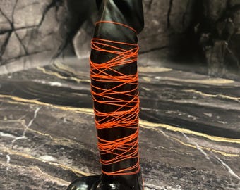 May include: A black candle shaped like a human body, wrapped in orange string.