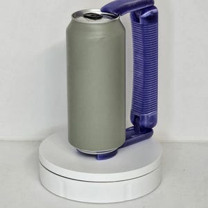 May include: A gray aluminum can with a silver top, held by a purple handle. The can is on a white rotating platform, and the handle is designed for easy gripping. The can is cylindrical and appears to be empty.