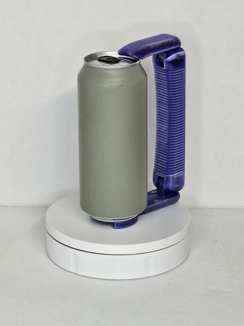 May include: A gray aluminum can with a silver top, held by a purple handle. The can is on a white rotating platform, and the handle is designed for easy gripping. The can is cylindrical and appears to be empty.
