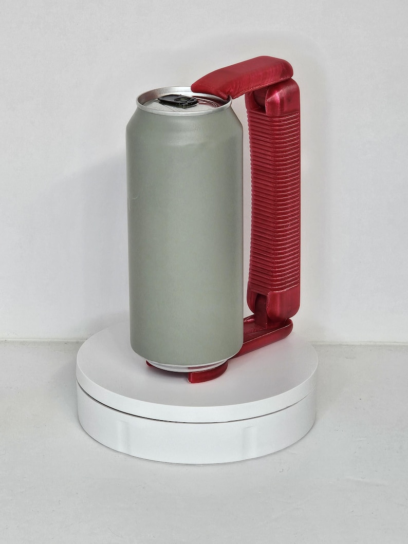May include: A gray aluminum can with a red plastic handle and opener. The can is on a white rotating platform. The handle is designed to make it easier to hold and open the can.