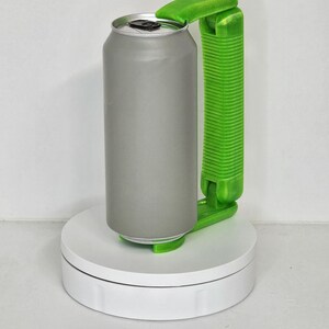 May include: A gray aluminum can with a silver top is held by a bright green can opener. The can opener has a handle and a lever to lift the can's lid. The can and opener are on a white rotating platform.