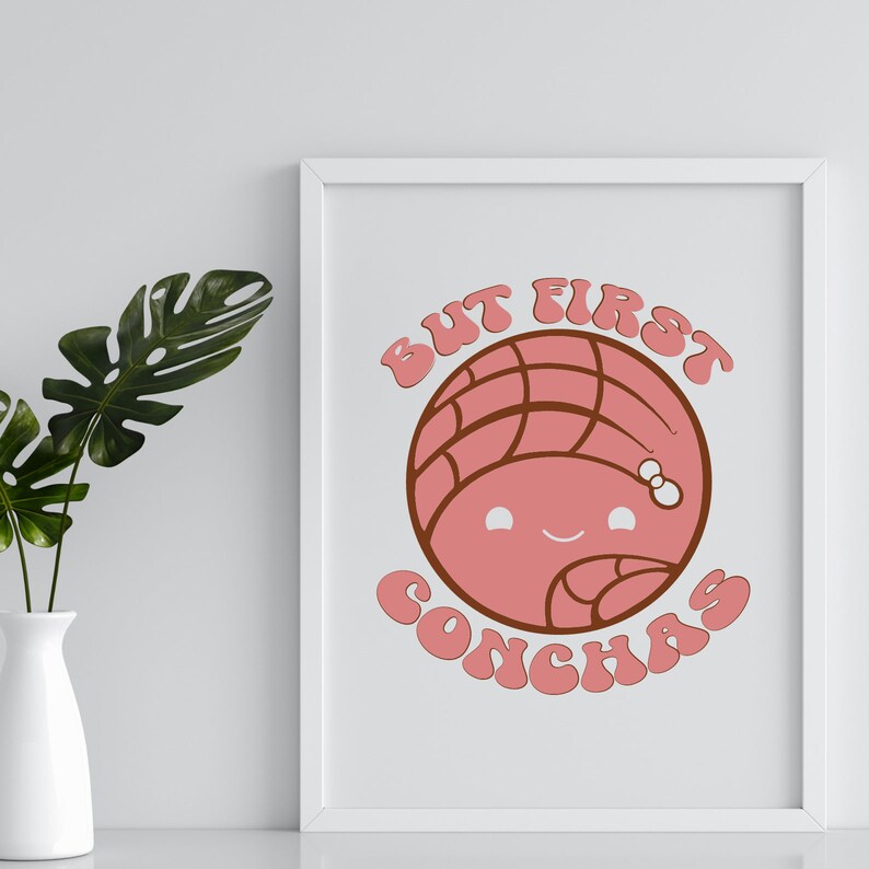 Op de afbeelding: Een wit ingelijst print met de tekst "But First Conchas" in een retro-lettertype. Een cartoon concha-gebak met een glimlachend gezicht bevindt zich in het midden van de print.