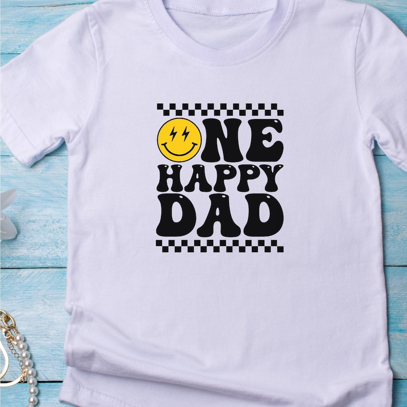 Puede incluir: Camiseta blanca con un gr&aacute;fico negro y amarillo que dice "ONE HAPPY DAD" con una carita sonriente.
