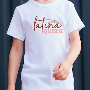 Op de afbeelding: Wit T-shirt met de tekst "latina QUEEN" in bruine en roze letters. Een kroonafbeelding bevindt zich boven het woord "latina".