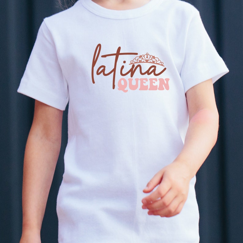 Op de afbeelding: Wit T-shirt met de tekst "latina QUEEN" in bruine en roze letters. Een kroonafbeelding bevindt zich boven het woord "latina".