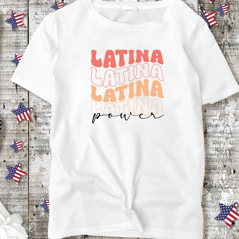 Op de afbeelding: Wit T-shirt met de tekst "LATINA POWER" in een gelaagde, retro fontstijl. De tekst is in roze en oranje tinten.