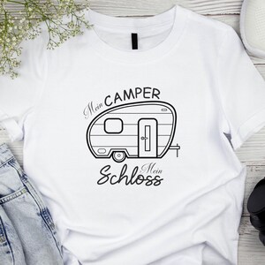 May include: White t-shirt with a black campervan illustration and the German text "Mein Camper Mein Schloss". The design shows a campervan with a door, window, and wheel. The t-shirt is made of a soft, comfortable material.