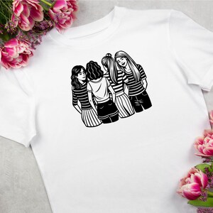 以下が含まれることがあります： 白地に黒と白のイラストがプリントされたTシャツ。4人の女性が寄り添って立っている。女性たちはスカートを履いており、互いに腕を組んでいる。