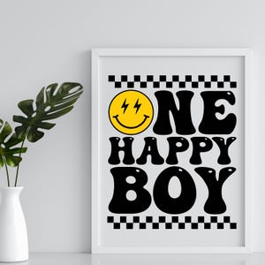 Puede incluir: Una impresi&oacute;n enmarcada en blanco con bordes a cuadros en blanco y negro. La impresi&oacute;n presenta una cara sonriente amarilla con rayos para los ojos y el texto "ONE HAPPY BOY" en negro, en fuente estilizada.