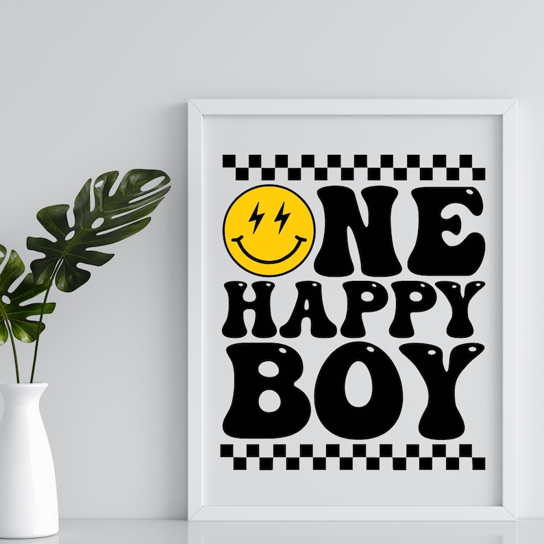 Puede incluir: Una impresi&oacute;n enmarcada en blanco con bordes a cuadros en blanco y negro. La impresi&oacute;n presenta una cara sonriente amarilla con rayos para los ojos y el texto "ONE HAPPY BOY" en negro, en fuente estilizada.
