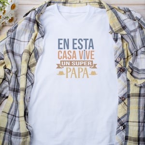 Puede incluir: Camiseta blanca con un gr&aacute;fico que dice "En esta casa vive un super papa" con una corbata y un sombrero a cada lado del texto.