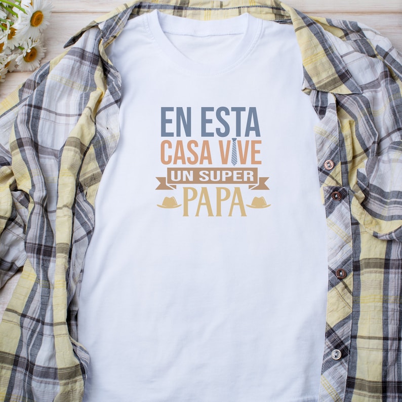 Puede incluir: Camiseta blanca con un gr&aacute;fico que dice "En esta casa vive un super papa" con una corbata y un sombrero a cada lado del texto.