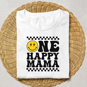 Puede incluir: Camiseta blanca con un borde de cuadros negros y blancos. El texto "ONE HAPPY MAMA" est&aacute; en negro con una cara sonriente amarilla con rayos para los ojos.