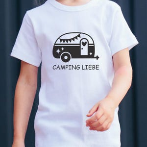 May include: White t-shirt with a black campervan graphic, a heart on the door, and the words "CAMPING LIEBE". The campervan has a banner and star details. The shirt is worn by a child.