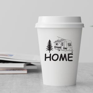 May include: White paper coffee cup featuring a black illustration of a caravan and a tree, with the word "HOME" beneath. The cup has a white lid and is on a light surface.