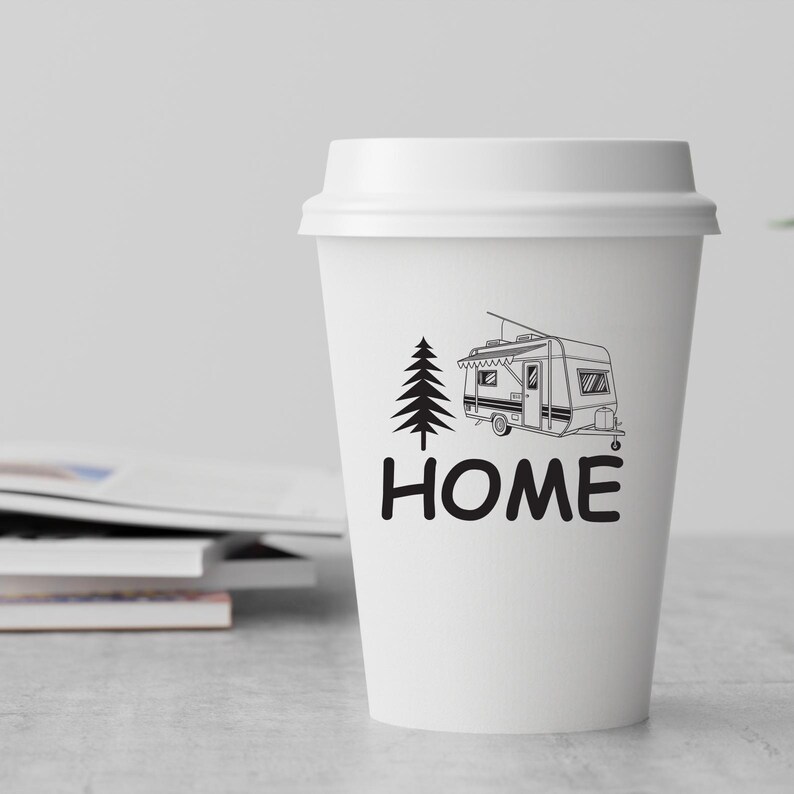 May include: White paper coffee cup featuring a black illustration of a caravan and a tree, with the word "HOME" beneath. The cup has a white lid and is on a light surface.