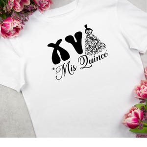K&ouml;nnte beinhalten: Wei&szlig;es T-Shirt mit schwarzem Grafikdesign. Das Design beinhaltet die Buchstaben "XV", eine Silhouette einer Frau in einem Kleid und die Worte "Mis Quince" in Schreibschrift. Rosa Blumen sind im Hintergrund zu sehen.