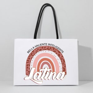 Op de afbeelding: Witte papieren tas met zwarte handvatten. De tas heeft een regenboogontwerp met een luipaardprint rand. De tekst "Bella Valiente Inteligente Latina" is gedrukt in een gestileerd lettertype.