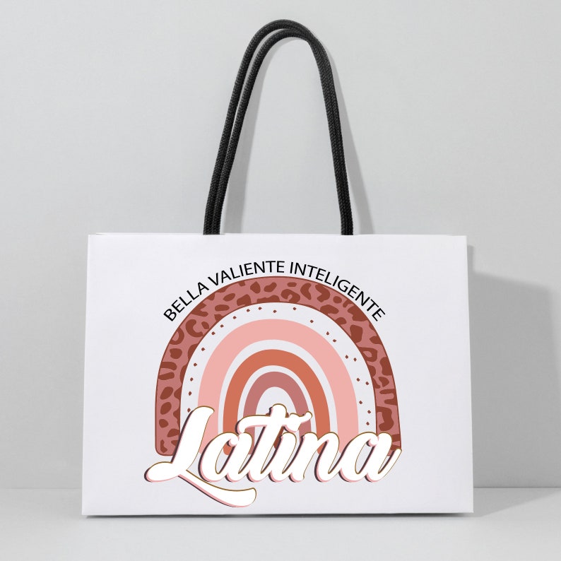 Op de afbeelding: Witte papieren tas met zwarte handvatten. De tas heeft een regenboogontwerp met een luipaardprint rand. De tekst "Bella Valiente Inteligente Latina" is gedrukt in een gestileerd lettertype.