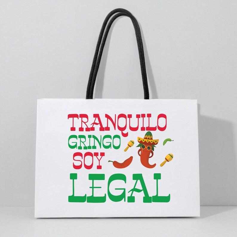 May include: White paper gift bag with black handles. The bag has a red and green graphic of a chili pepper wearing a sombrero and sunglasses. The text "Tranquilo Gringo Soy Legal" is printed on the bag.