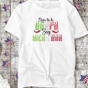 May include: White t-shirt with a green, white, and red graphic that says "Deja tu lo GUAPA Soy MEXICANA" with red chili peppers on either side of the word "Soy".