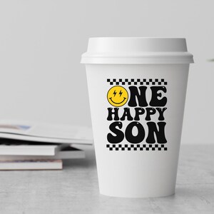 Puede incluir: Vaso de caf&eacute; blanco para llevar con un borde de cuadros negros y blancos alrededor del texto "ONE HAPPY SON" con una cara sonriente amarilla con rayos para los ojos.