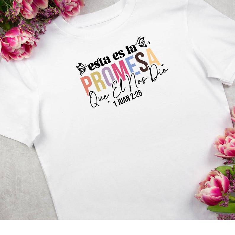 May include: White t-shirt with a colorful graphic that says "Esta es la Promesa Que El Nos Dio + 1 Juan 2:25".