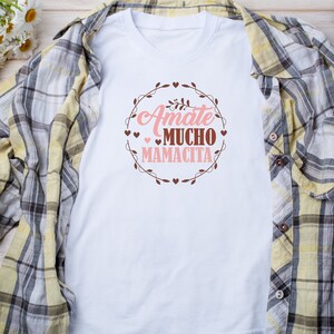 Op de afbeelding: Wit T-shirt met een bruin kransontwerp en de tekst "Amate mucho Mamacita" in roze.