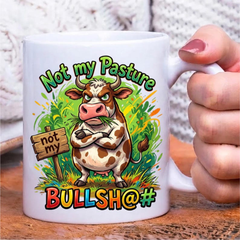 Pode incluir: Uma caneca de cer&acirc;mica branca com uma ilustra&ccedil;&atilde;o colorida de uma vaca castanha e branca com os bra&ccedil;os cruzados, em p&eacute; na relva verde. O texto diz Not my Pasture acima da vaca, not my numa placa de madeira e BULLSH@# na parte inferior.