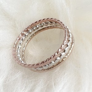 May include: Three intertwined rings, one silver and two rose gold, with a beaded design.
