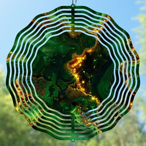 May include: A green and gold metal wind spinner with a swirling design. The spinner has a circular shape and is made of multiple layers of metal.
