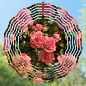 May include: A metal wind spinner with a circular design featuring a pink rose pattern. The spinner has multiple layers of metal that create a swirling effect when it spins in the wind.