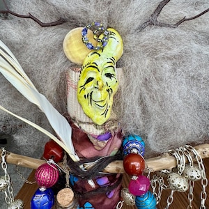 May include: A whimsical handmade doll with a yellow face mask, gray hair, and colorful beads. The doll is adorned with a small glass bottle labeled "Yellow Agate".