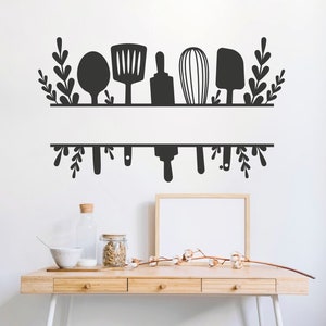 Pode incluir: Adesivo de parede de utensílios de cozinha em preto e branco com uma prateleira e utensílios pendurados, incluindo uma espátula, um rolo, um batedor e uma colher. O adesivo está em uma parede branca sobre uma mesa de madeira com um vaso, um frasco e uma tigela.