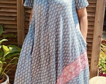 May include: A blue and white patterned maxi dress with a pink and white trim. The dress has a V-neck and short sleeves. The model is wearing the dress with brown sandals.