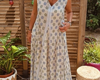 May include: A white maxi dress with a green and blue floral pattern. The dress has a V-neckline and sleeveless design. The model is wearing brown sandals.