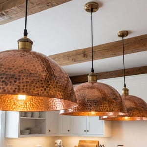 Hand-hammered copper pendant light with a large dome shape and warm reddish-orange metallic finish.