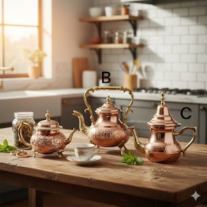 Peut inclure: Trois théières en cuivre avec des motifs ornés et des poignées en laiton sont posées sur une table en bois. Une tasse et une soucoupe sont devant la théière du milieu. Les théières sont de tailles et de formes différentes, avec des motifs complexes.