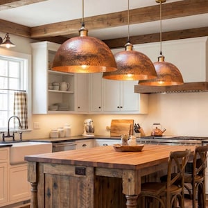 Three identical copper dome lights hanging at different heights over a wooden kitchen island with white cabinets.