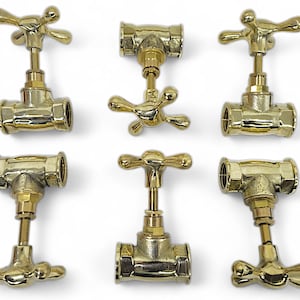 Puede incluir: Seis válvulas de grifo de color latón con manijas en forma de cruz están dispuestas sobre una superficie blanca. Las válvulas tienen un cuerpo en forma de T y están diseñadas para aplicaciones de fontanería. La imagen muestra los detalles de los accesorios.