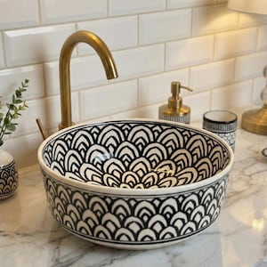May include: A black and white patterned ceramic vessel sink with a gold faucet. The sink features a repeating arch design. Other bathroom accessories include a soap dispenser and a small vase.