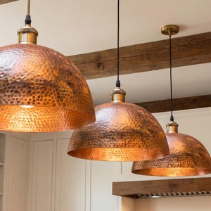 Dark-colored dark bronze patina copper light fixture against a rustic brick wall in a dining room.