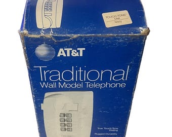 Pode incluir: Uma caixa de papelão azul para um telefone de parede AT&T Traditional. A caixa apresenta texto em branco, uma ilustração de um telefone de parede com teclado na cor marfim e uma etiqueta no painel superior indicando a cor marfim.
