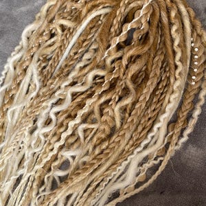 Thin double-sided synthetic dreadlocks with extensions, in beige and blond tones.