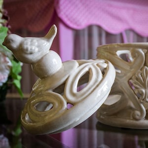 以下が含まれることがあります： 鳥の置物付きのオフホワイトのセラミックジャー。ジャーは、花柄とスクロール模様のオープンワークデザインです。ふたは部分的に開いています。装飾的な家の装飾。