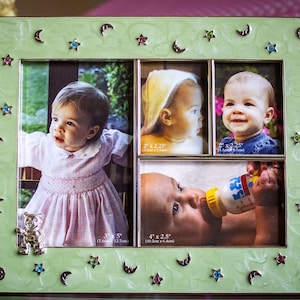 May include: A light green multi-photo frame with four openings, each displaying a baby photo. The frame is decorated with silver moons, stars, and colorful gems. A silver teddy bear is at the bottom left.