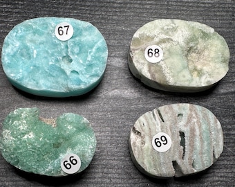 May include: Four polished, oval-shaped gemstones in shades of blue, green, and gray. Each stone has a unique texture and pattern. Small white stickers with numbers 66, 67, 68, and 69 are affixed to each stone.
