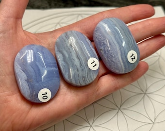 May include: Three polished blue lace agate stones with distinct white banding. Each oval-shaped stone features a smooth, glossy surface and a small white circular sticker labeled with the numbers 10, 11, and 12 respectively for identification.