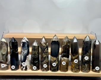 May include: Ten polished stone towers arranged in a row on a tiered wooden display stand. Each tower features unique patterns of black, brown, and cream colors. Small white circular stickers numbered 33 through 42 are attached to each stone tower.